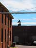 A pipe runs between 2 buildings in the Saxonville Mills. The bell tower is in the cackground.